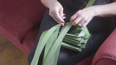 shot in slow motion of a woman weaving a basket with green plant leaves.