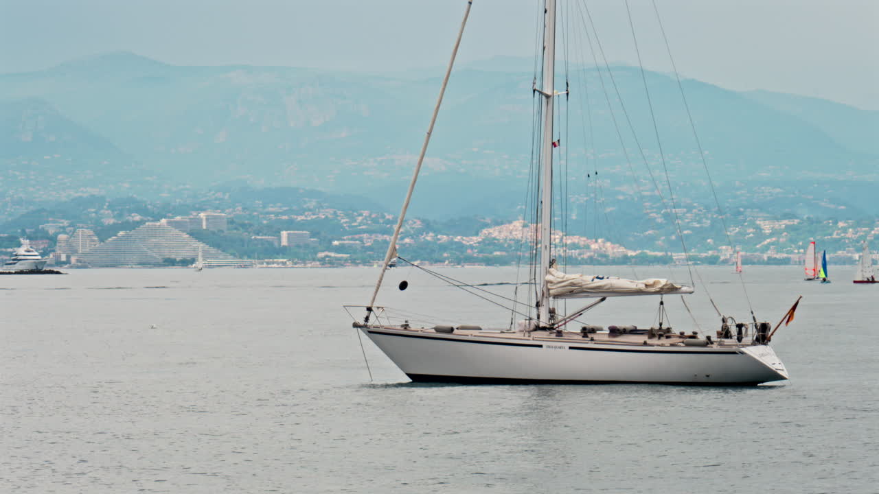 Villeneuve-Loubet, Francia - 7 maggio 2025: una barca bianca con la bandiera tedesca attraccata sul mare con la Marina Baie des Anges sullo sfondo