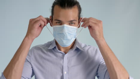 smiling millennial man takes of and puts on face mask, giving thumbs up