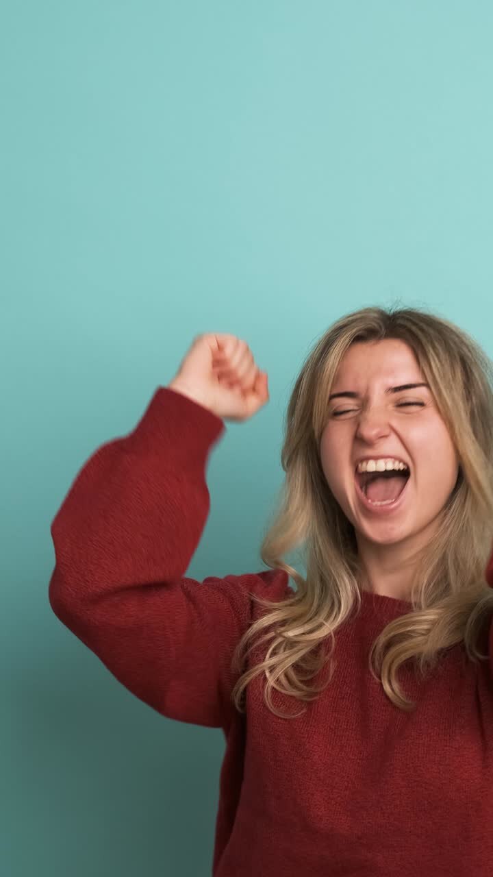 Giovane donna di successo che stringe i pugni in uno studio blu