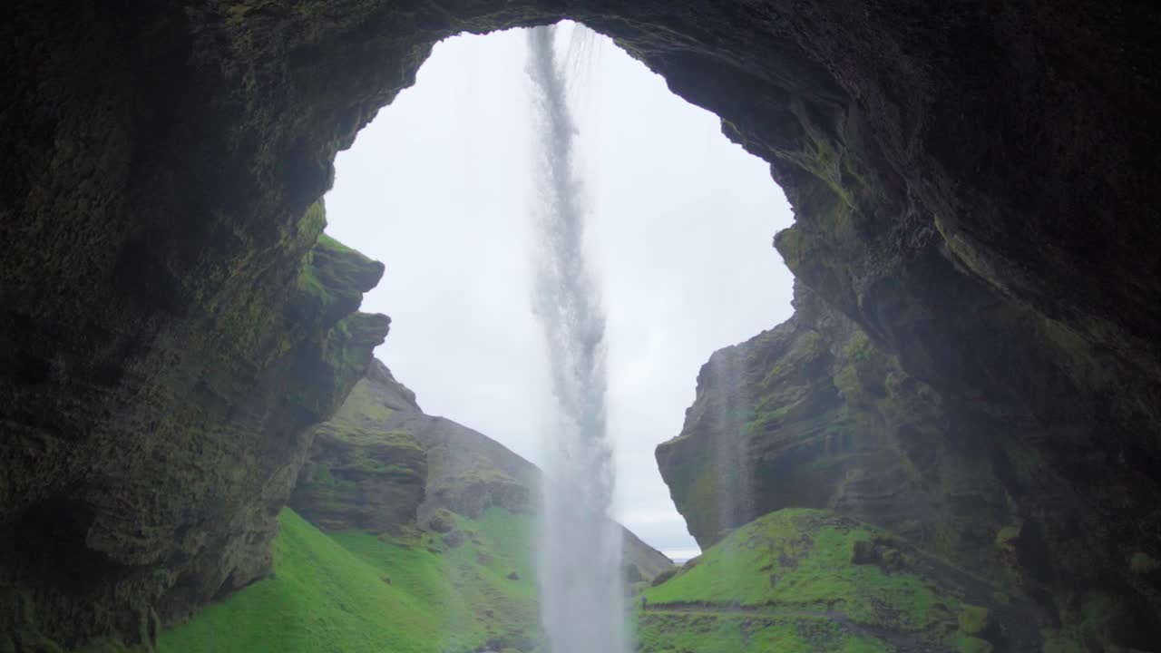 una vista desde detrás de una cascada en islandia, mirando hacia el cañón más allá - cámara lenta
