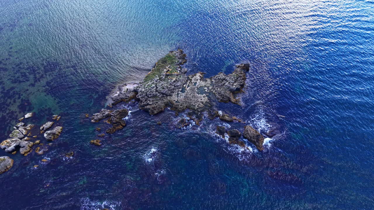 Vista aérea deslumbrante de uma ilha rochosa cercada por águas azuis tranquilas sob um céu limpo ao meio-dia