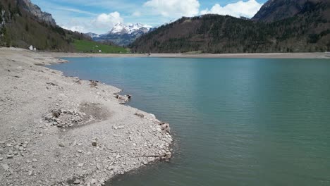 aerial forward view of shoreline of an alpine lake with mountains surrended