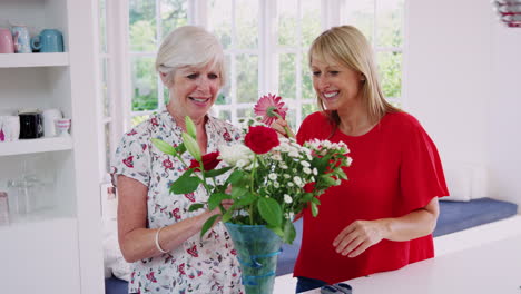 Senior-woman-and-adult-daughter-flower-arranging-in-kitchen