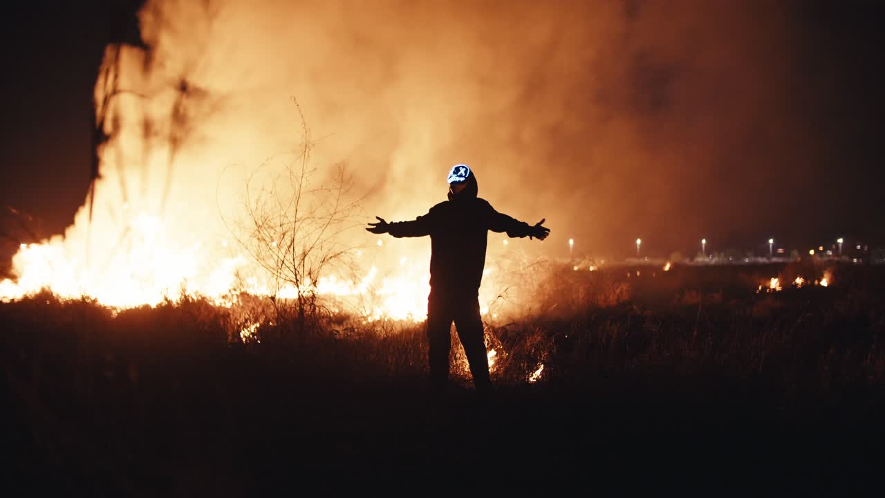 persona de pie frente a un incendio forestal por la noche