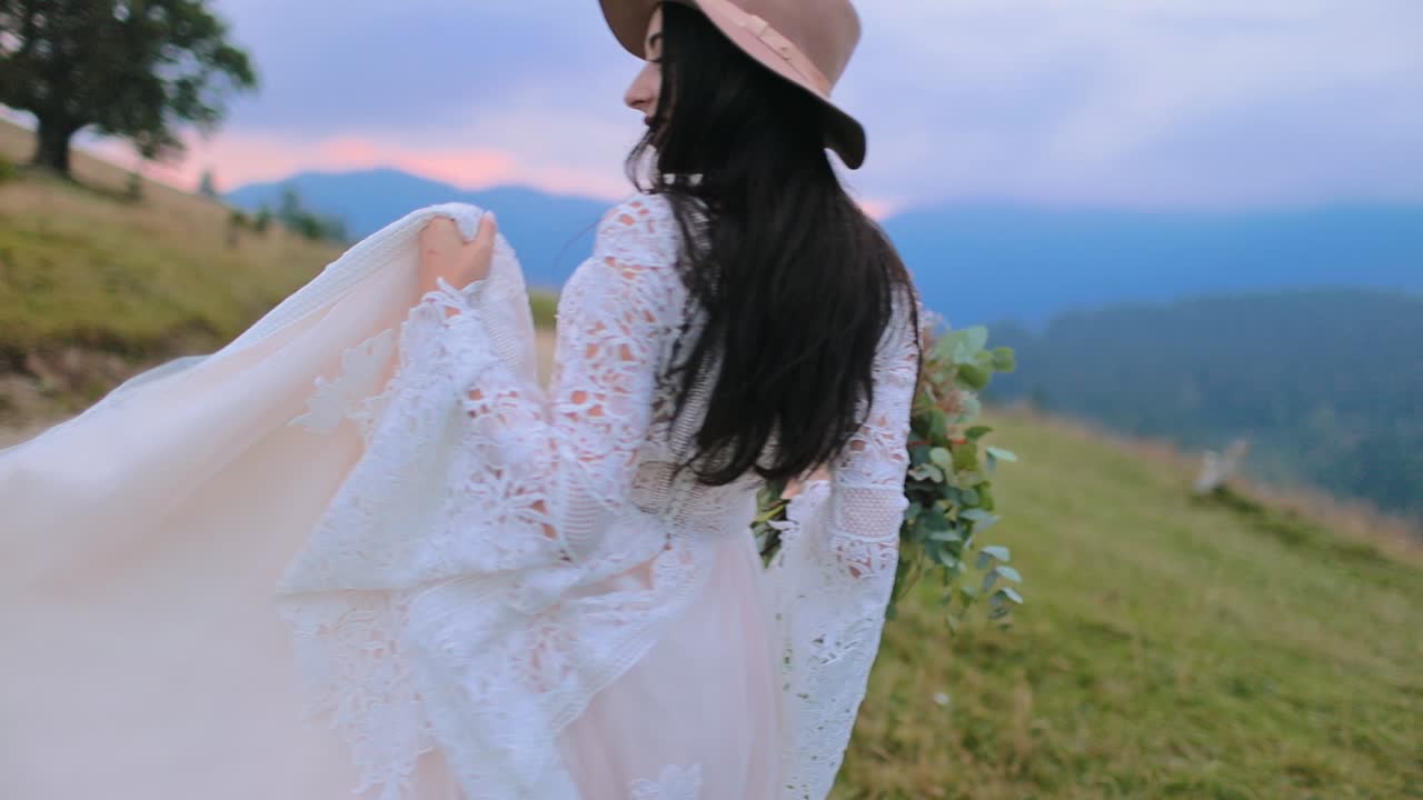 Pretty young woman posing at camera. Beautiful girl in hat and magnificent white dress among nature. Happy bride at sunset.