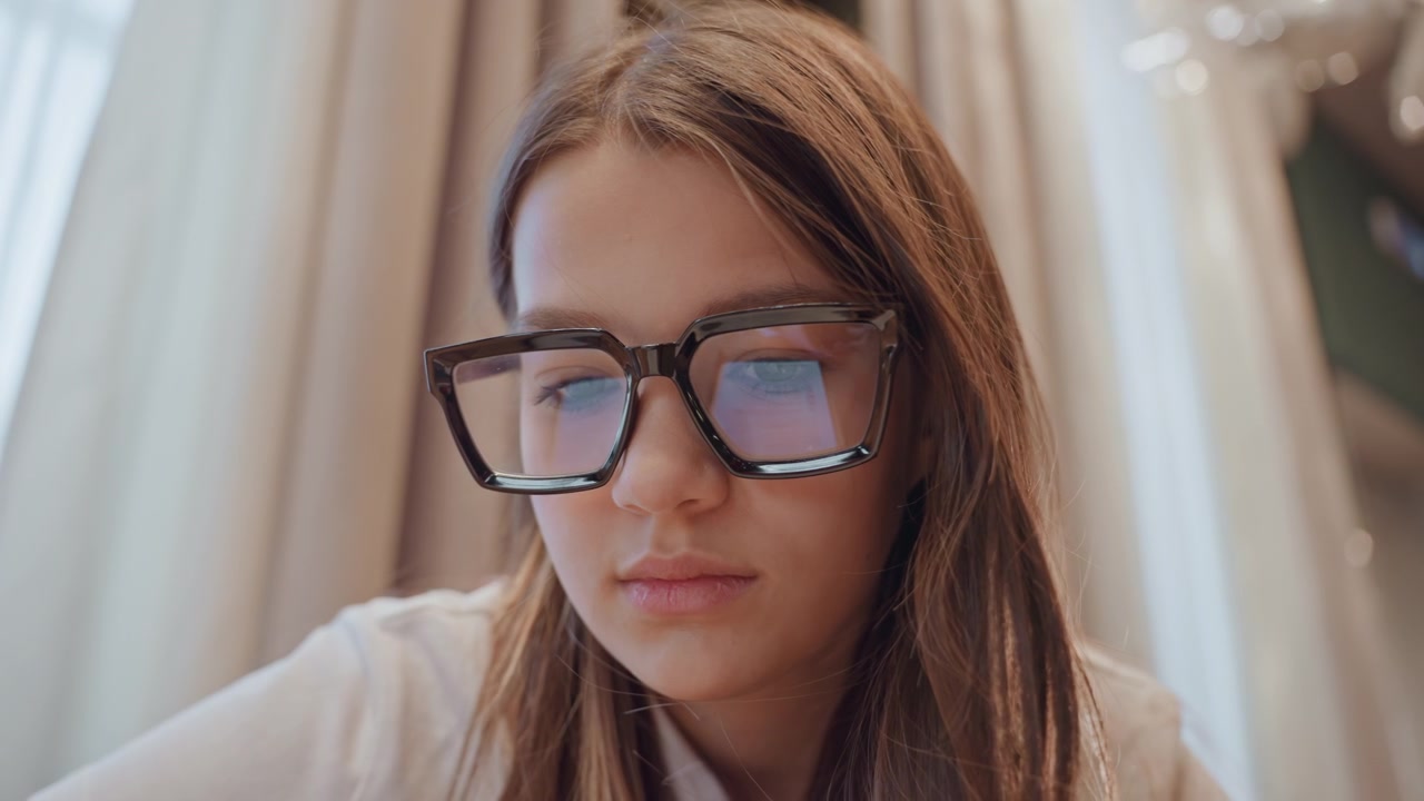 Ragazza adolescente che interagisce con il suo dispositivo digitale. Studentessa che si concentra durante una sessione di apprendimento online serale. Giovane donna con gli occhiali che lavora diligentemente al suo laptop in un tranquillo ambiente serale.