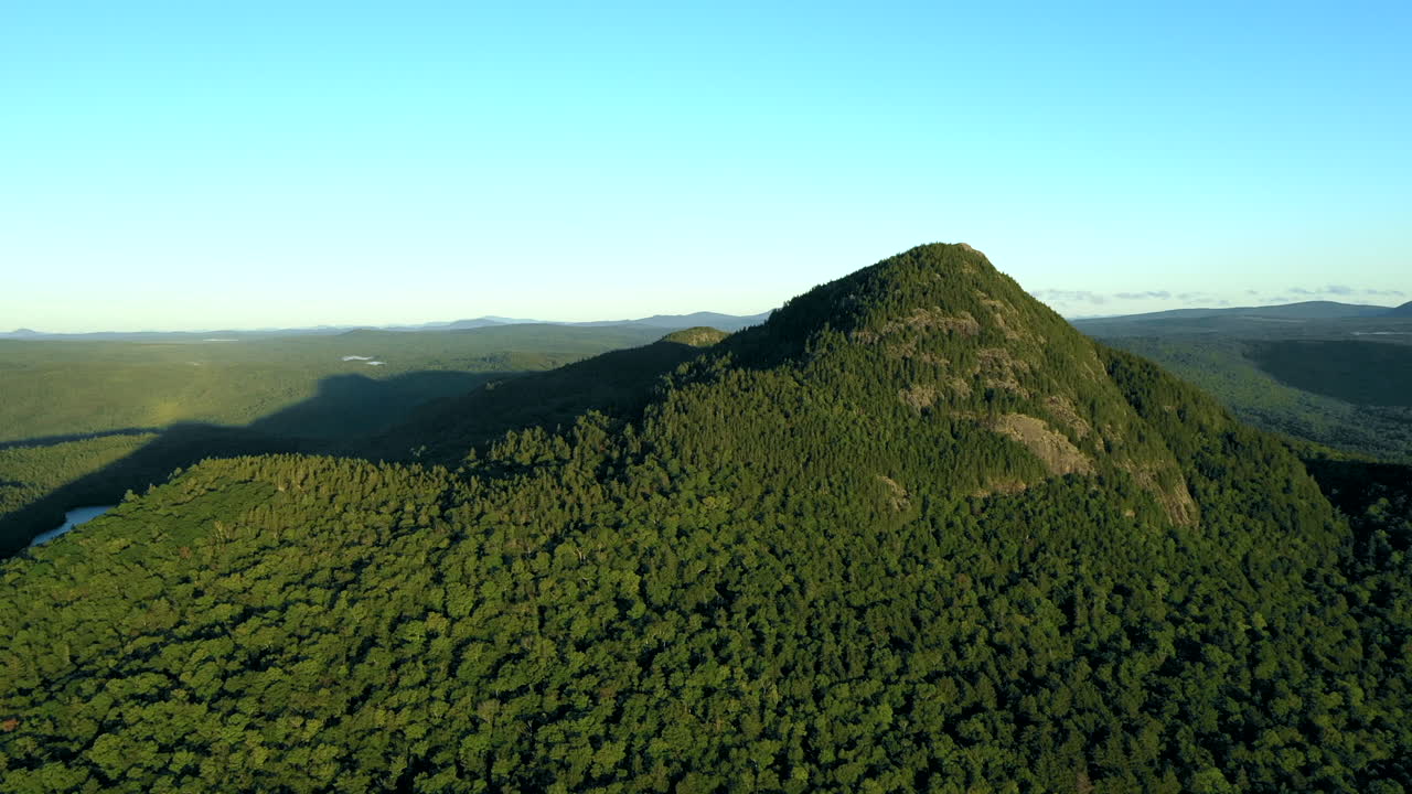 toma aérea de drones de la montaña boreal que revela un lago azul a la sombra del pico entre el espeso bosque verde del desierto de maine