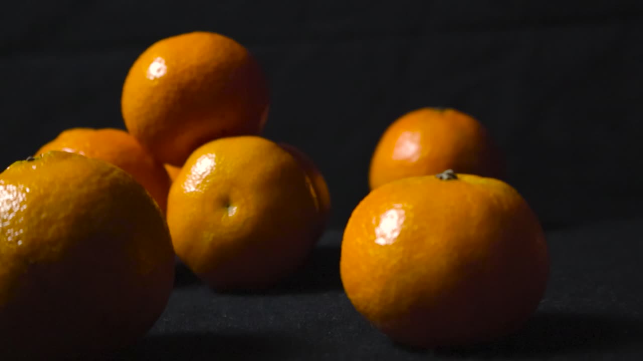 imágenes cercanas de clementinas o mandarinas naranjas vibrantes en un fondo negro oscuro mientras las imágenes giran a su alrededor. el primer plano está ligeramente borroso y las frutas de fondo están en foco agudo.