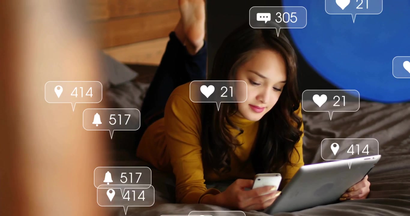 woman lying on bed using smartphone and tablet showing floating hearts comment icons for marketing