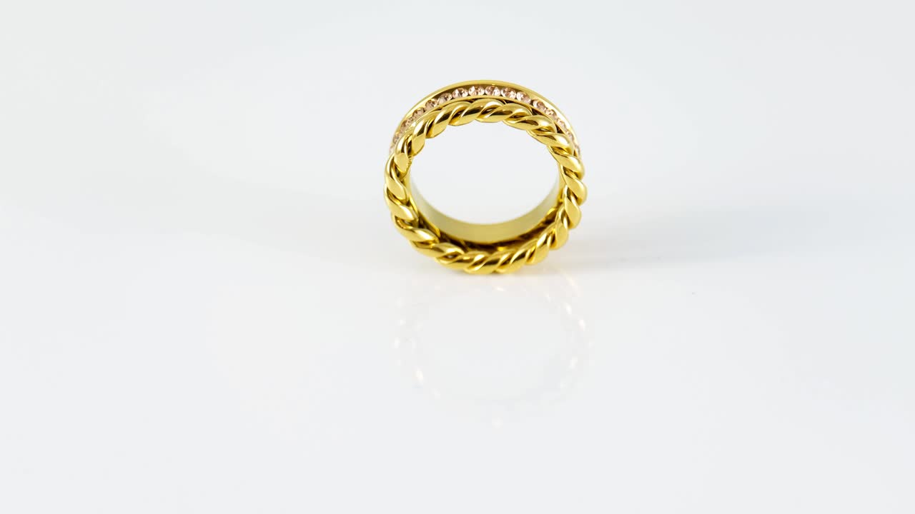 Rotierender goldener, geknoteter, funkelnder Doppelring aus Gold mit Zirkonen auf weißem Hintergrund. Schönes Valentinsgeschenk
