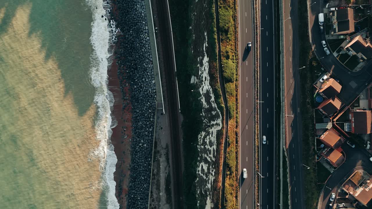 Birdseye descent over coastal freeway with crashing waves and seaside homes