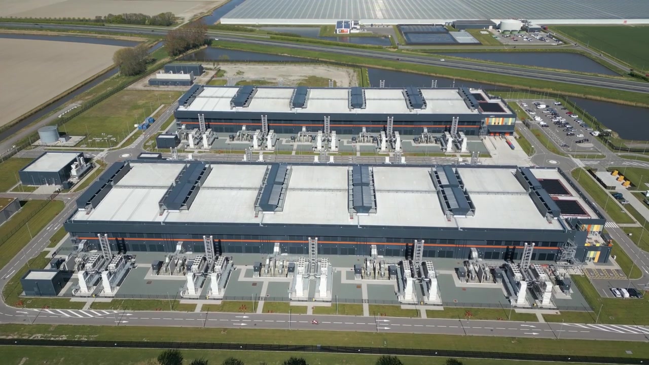 Drone shot of a large hyperscale data center campus with modern industrial architecture, cooling infrastructure and surrounding Dutch landscape in the Netherlands.
