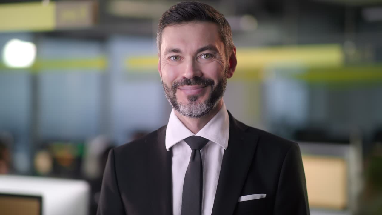 retrato de un hombre de negocios adulto jefe de pie en la oficina sonriendo mirando a la cámara mientras los empleados están ocupados trabajando en el fondo