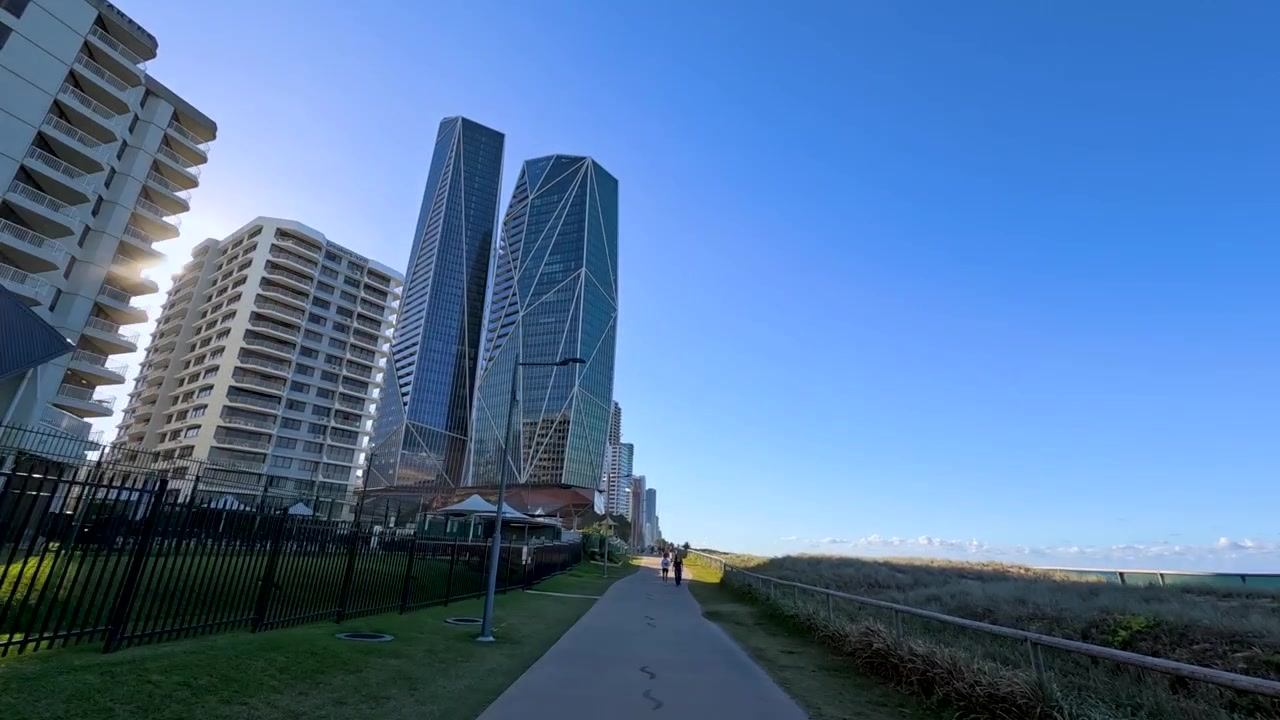 Pessoas caminhando e andando de bicicleta em um caminho costeiro perto de arranha-céus modernos