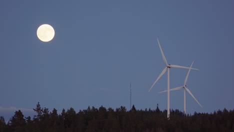 slow motion, zoom out - wind turbines spin next to a rising full moon