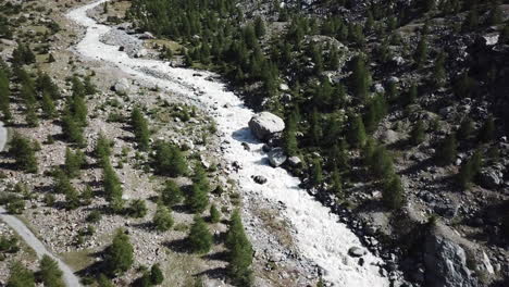 Swiss-alps-mountain-stream,-rocky-river-and-fir-forest-in-a-valley,-drone-aerial-view,-push-out