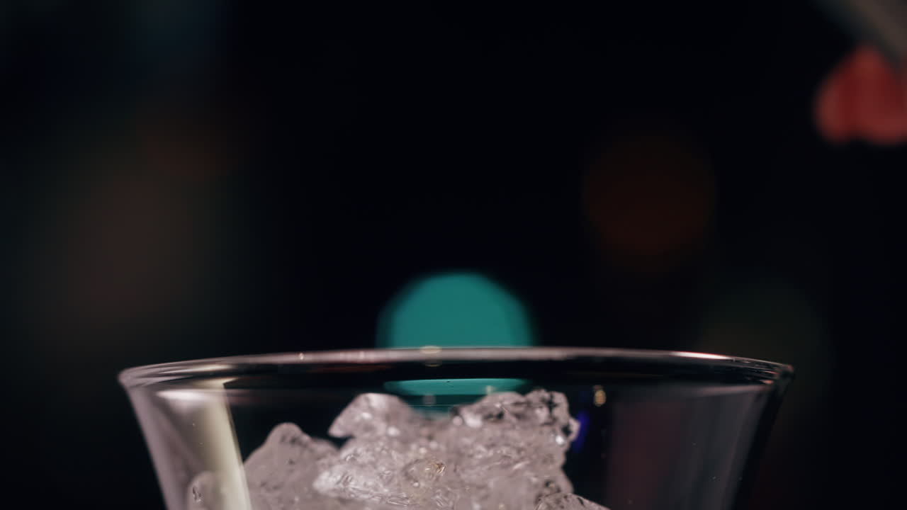 Bevanda alcolica versata su cubetti di ghiaccio cristallini in un bicchiere da cocktail su uno sfondo scuro.