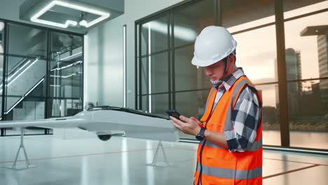ingeniero comprobando el teléfono inteligente en una oficina moderna con un avión no tripulado