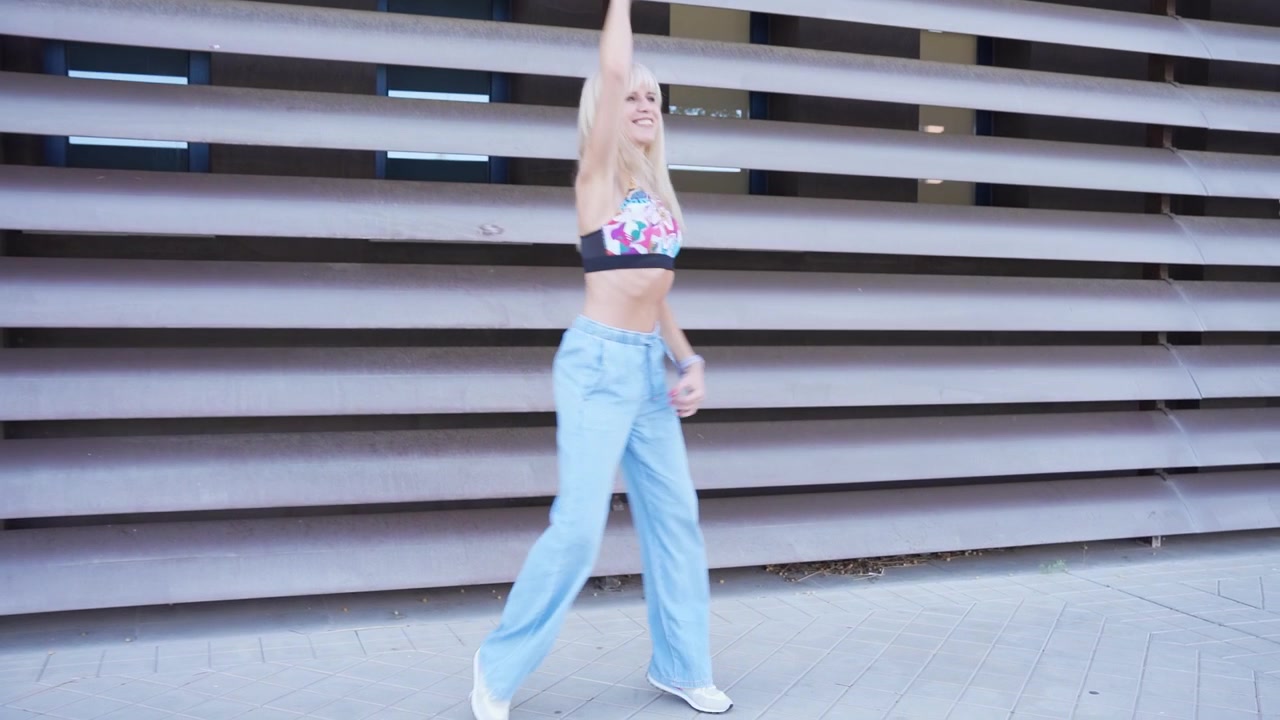 En ung kvinde danser i byen iført en crop top og jeans, der udstråler en sorgløs stemning