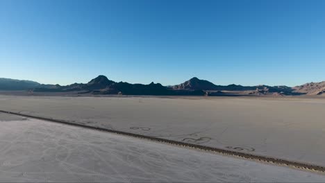 car tracks in the salt and a car driving across the bonneville salt flats causeway are seen from above by drone