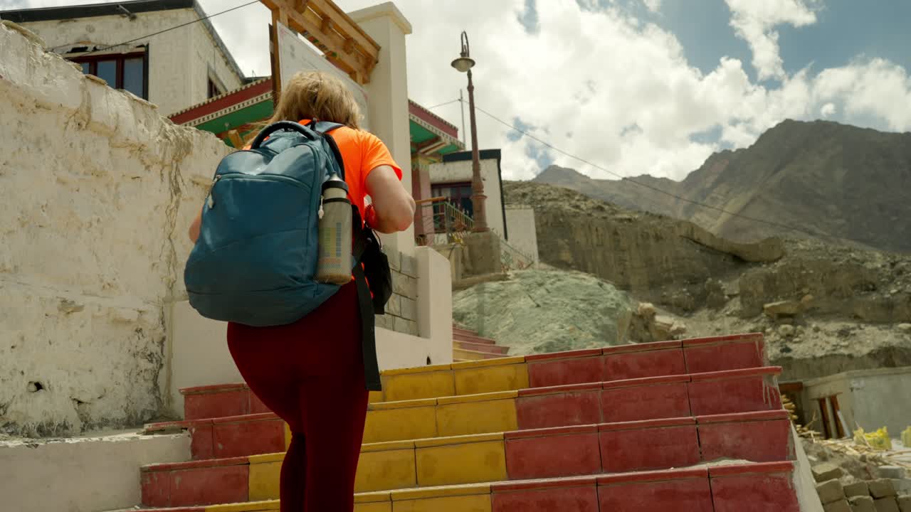el turista mayor sube los coloridos escalones del templo, explorando los monasterios budistas en ladakh. el jubilado en vacaciones de aventura en las montañas del himalaya visita el impresionante templo de gompah en una remota zona panorámica.