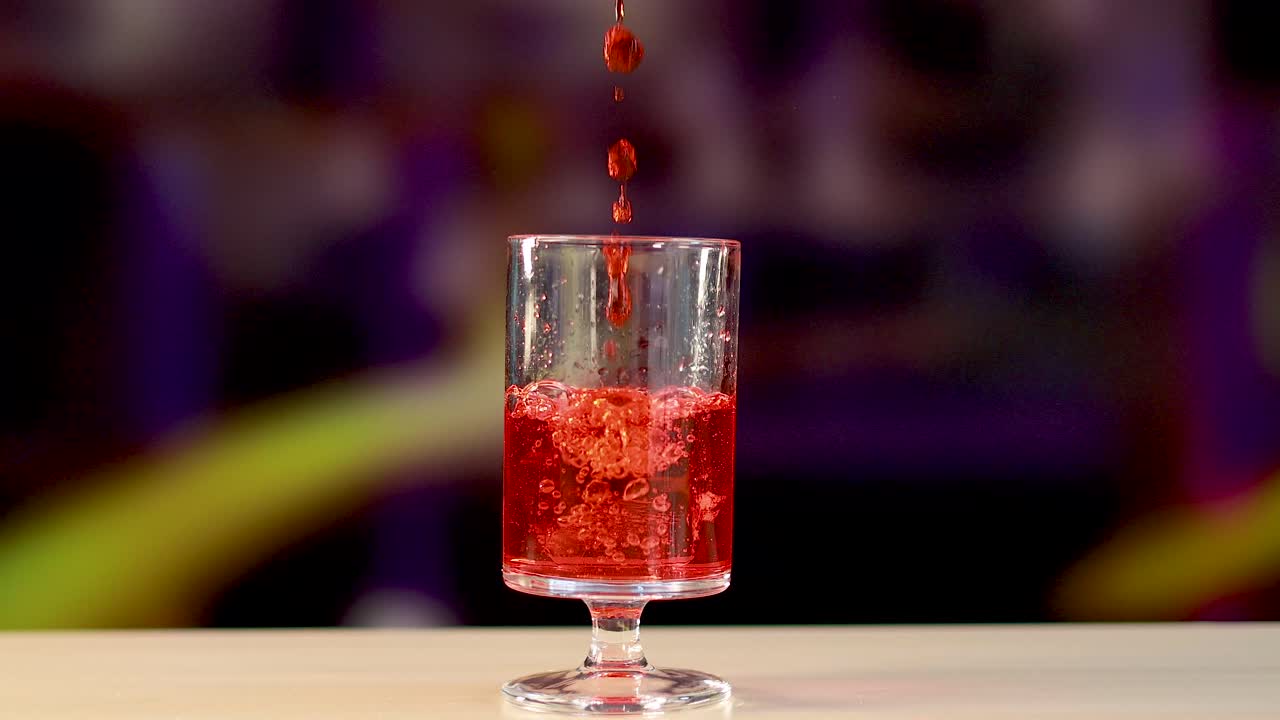 A Negroni cocktail is poured over ice in a clear glass, set against a vibrant background with dynamic lighting