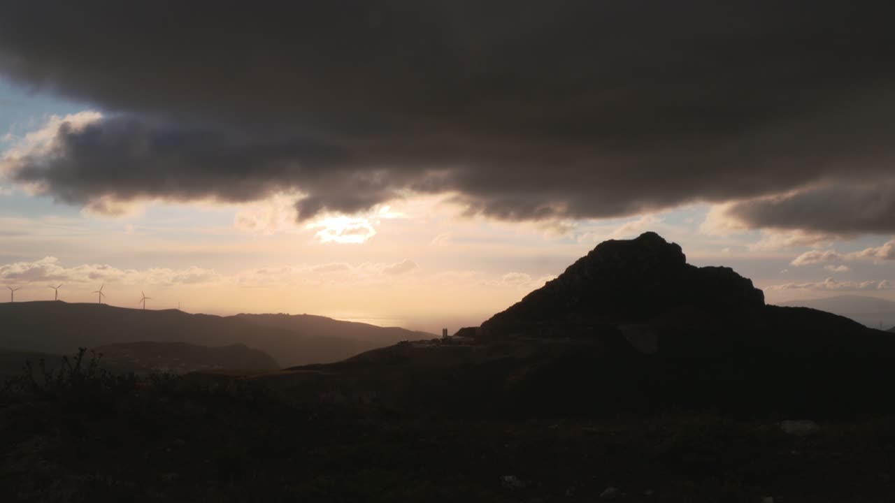 Dramatic sunset over Moroccan mountain landscape with wind turbines in distance under dark clouds creating cinematic nature and renewable energy scene