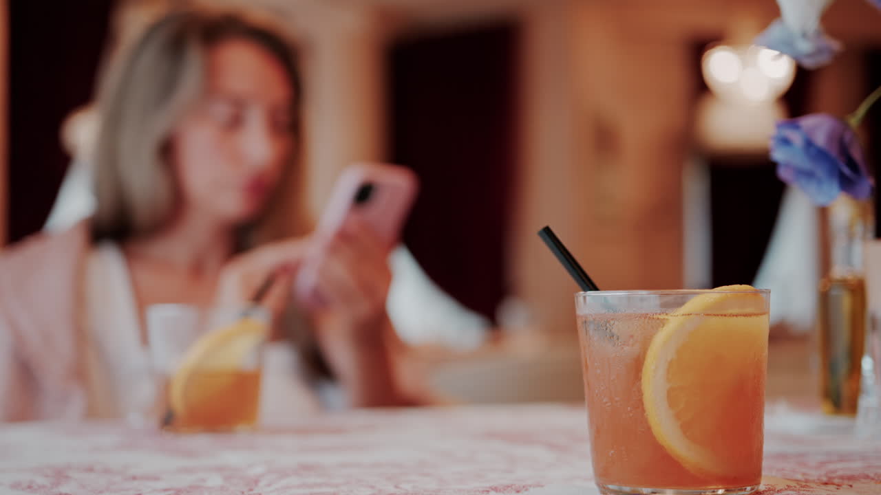 Close up of an orange cocktail on a table with a woman on the background at a restaurant