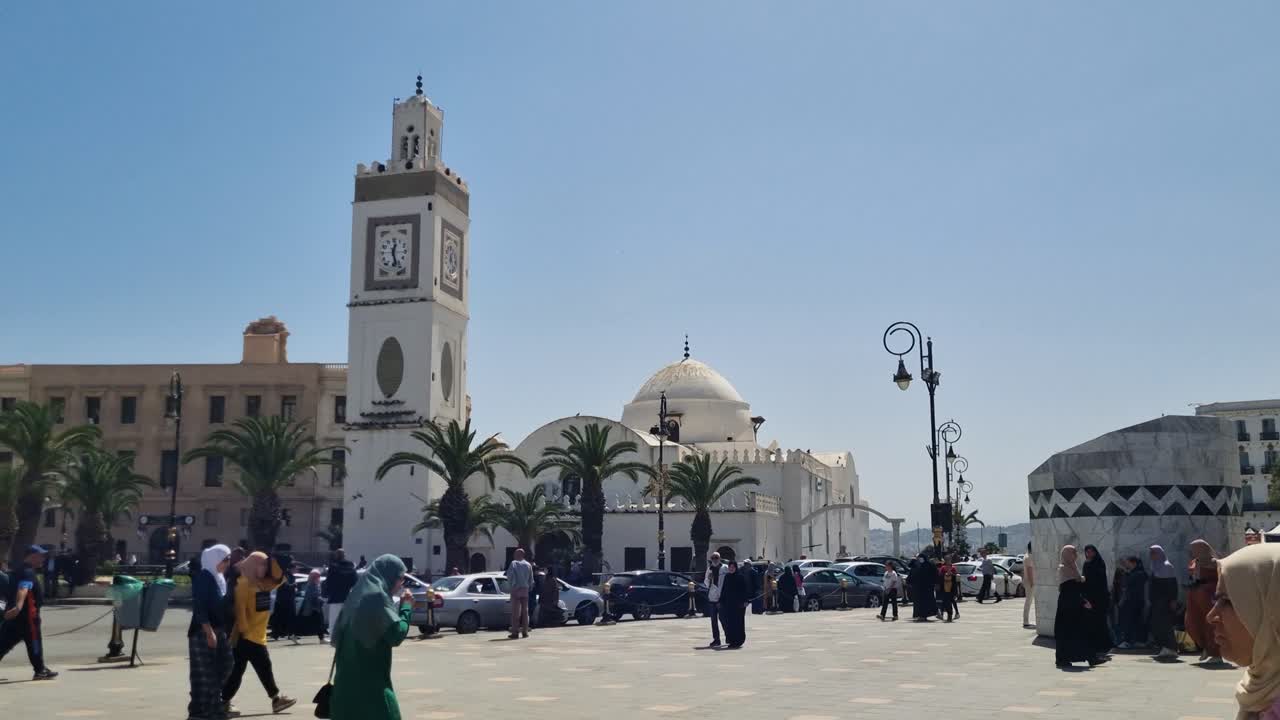 Local people in hijab passing square in front of Djama a al-Djedid mosque on a sunny day with blue sky in central Algiers, Algeria