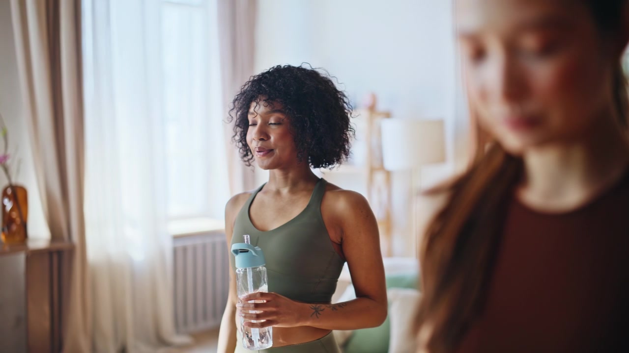 Donna asiatica che beve acqua dopo un allenamento a casa. Primo piano di una pausa idratazione fitness.