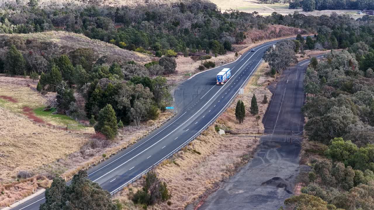 Aerial view of a semi truck traveling along a winding rural highway through dry bushland near Coonabarabran, NSW, under natural daylight with steady camera movement