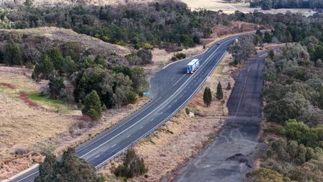 aerial view of a semi truck traveling along a winding rural highway through dry bushland near coonabarabran, nsw, under natural daylight with steady camera movement