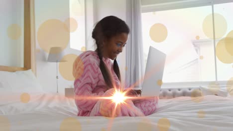 Animation-of-light-spots-and-trails-over-african-american-girl-using-laptop