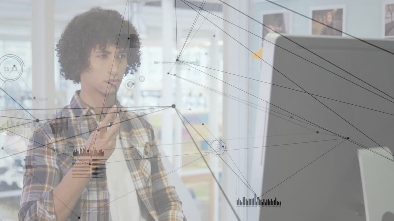 tech designer using stylus on monitor in open office, with network overlay graphics data charts