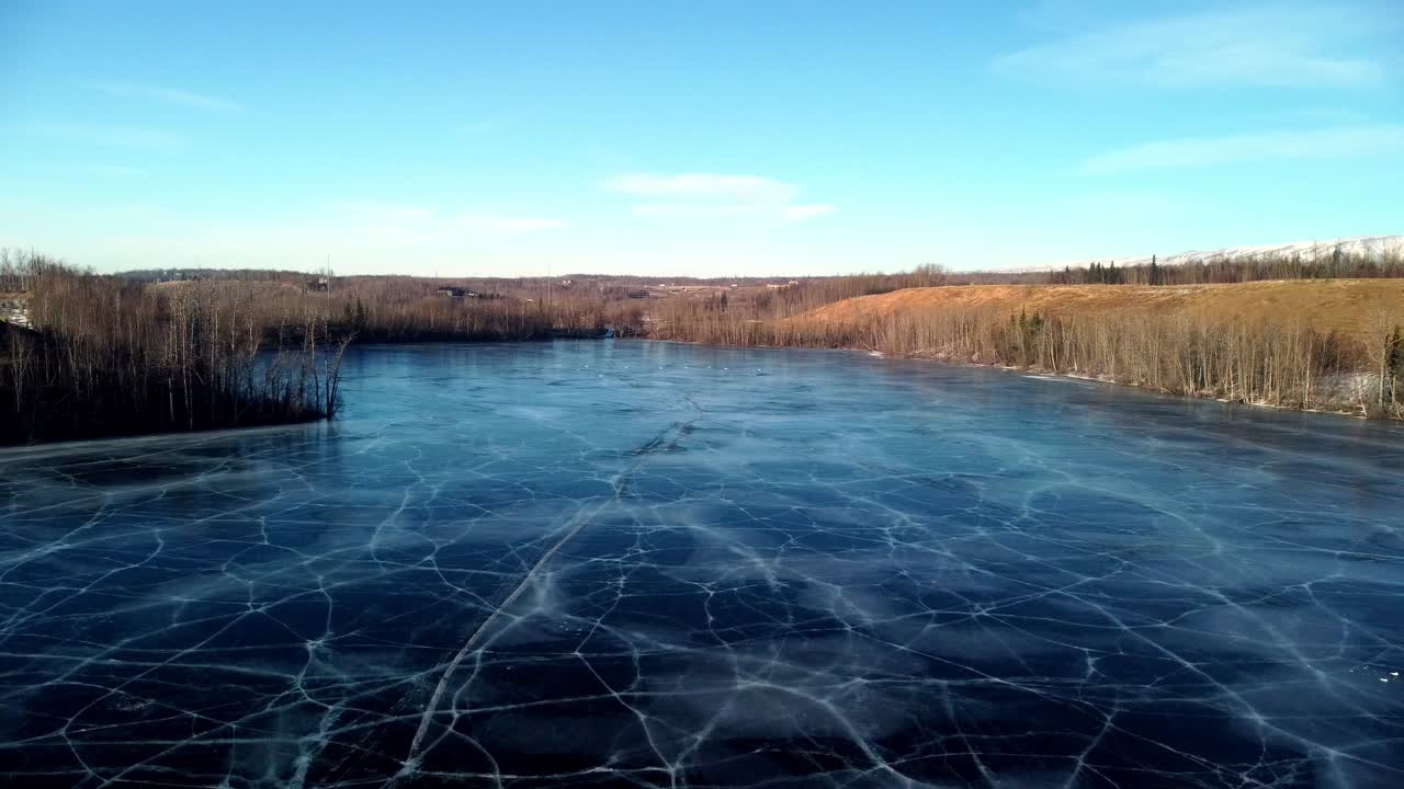 Lavtflygende drone flyr tjue til tretti fot over den frosne overflaten av Matanuska Lake, reiser i motsatt retning over det enorme området. Dypblå is med slående grå høydepunkter.