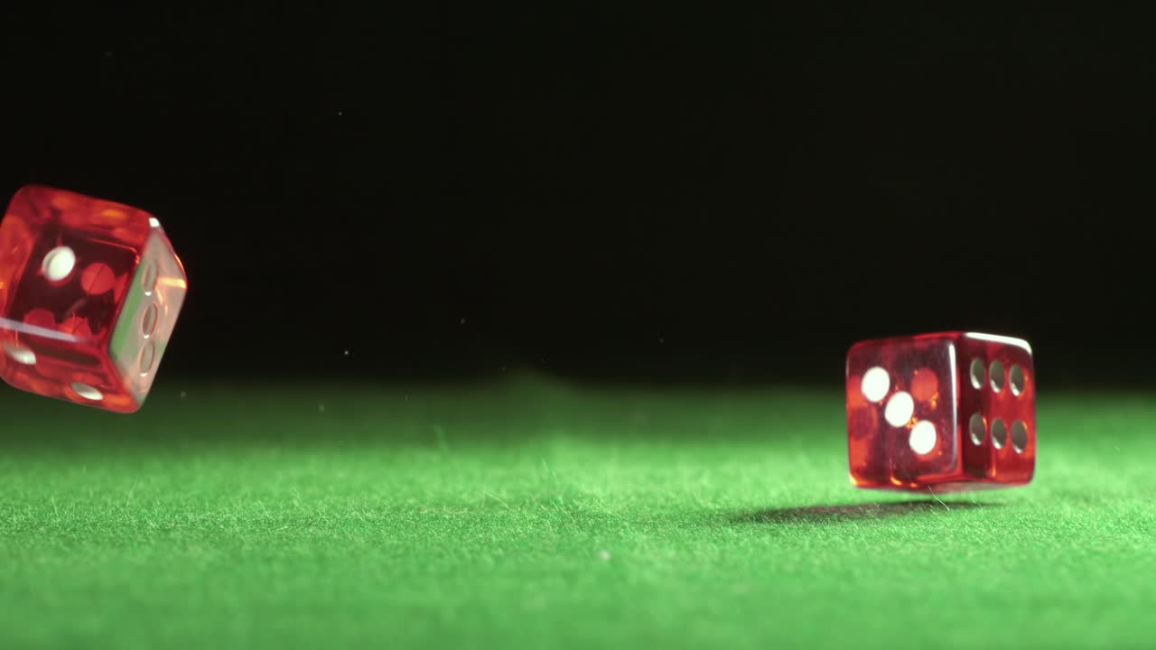 Røde terninger, der falder og hopper på et grønt bord med en mørk baggrund. Optaget med super slow motion-kamera ved 1000 fps.