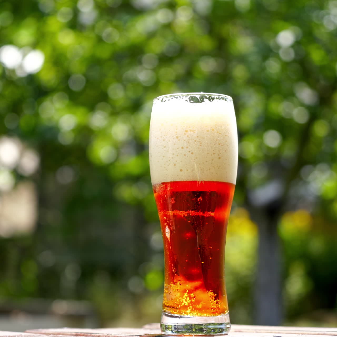 Cold beer in a glass with white foam. Craft beer in a glass with small bubbles inside. Cool brown beverage on a table outdoors. Close-up.