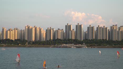 Gente-Irreconocible-Haciendo-Windsurf-En-El-Río-Han-En-Seúl-En-La-Impresionante-Y-Pintoresca-Puesta-De-Sol-Sobre-El-Complejo-De-Apartamentos-De-Alto-Nivel-De-Jamsil