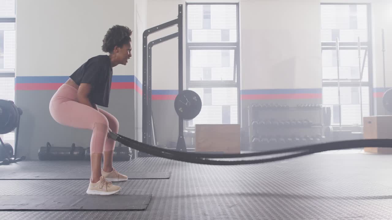 video de una mujer afroamericana decidida trabajando en un gimnasio con cuerdas de lucha.