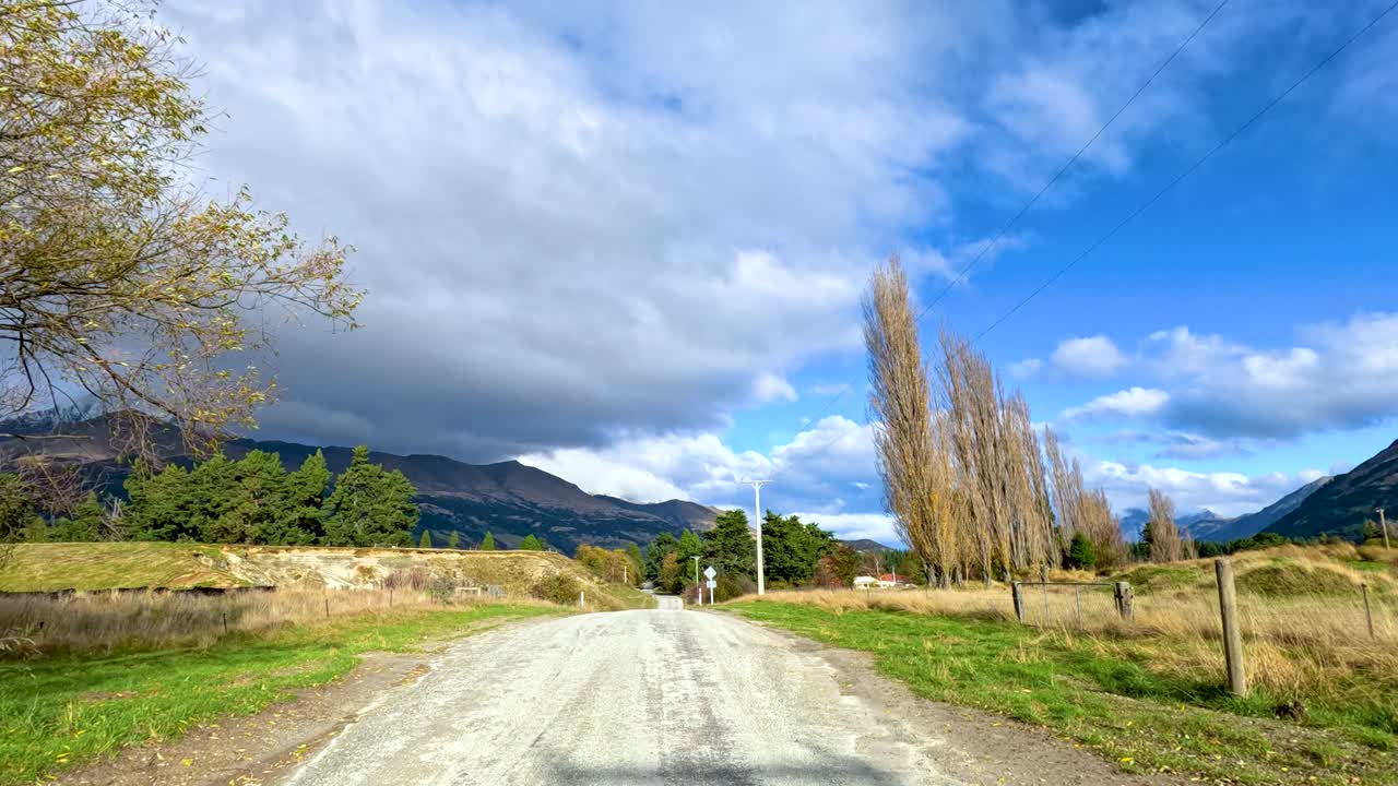 Vehicle travels rural gravel road with mountain views, bright daylight, and steady forward camera movement