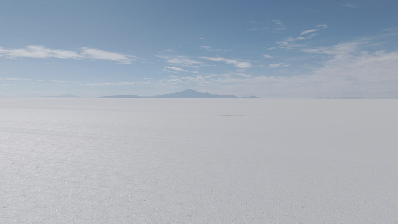 Drone shot flying above the dry salt flats in Bolivia Uyuni on the cloudy day with some small hills in the background LOG