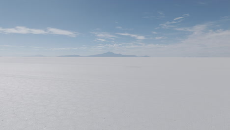 drone shot flying above the dry salt flats in bolivia uyuni on the cloudy day with some small hills in the background log