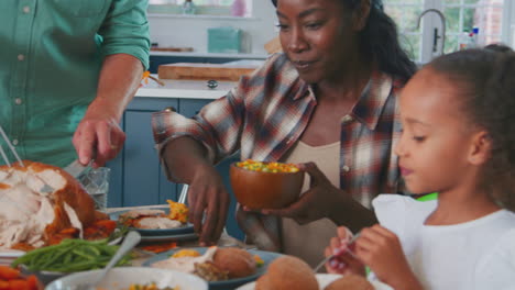 grandfather carves and serves turkey as multi-generation family celebrating thanksgiving with meal
