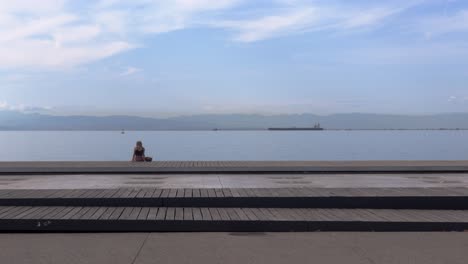 mujer sentada en un muelle mirando hacia el océano desde el puerto con barcos en el fondo