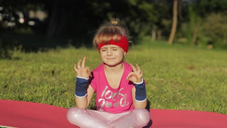 niño sentado en una alfombra y realizando meditación de yoga al aire libre en el parque. niña haciendo ejercicios de yoga