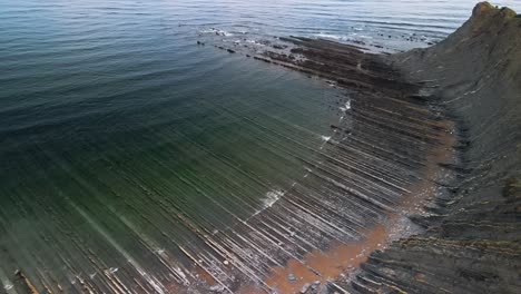 Playa-de-Sakoneta-Basque-Spain,-flysch-geologic-formations-stretch-out-into-ocean,-panoramic-aerial-static