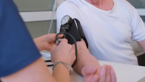 zoom in shot of young male therapist in white coat measuring blood pressure of senior patient in ward of clinic
