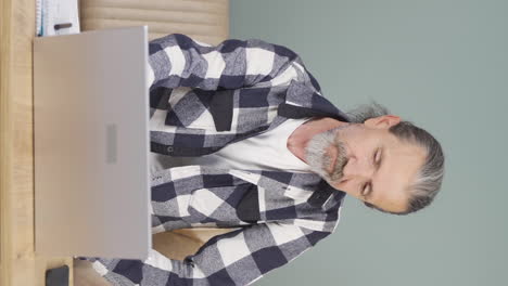 vertical video of old man looking at laptop is unmotivated and bored.