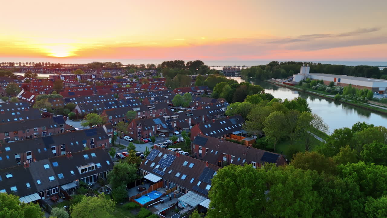 Flying over the peaceful lake at sunset. Approaching the picturesque green village with similar houses. Countryside in the Netherlands.